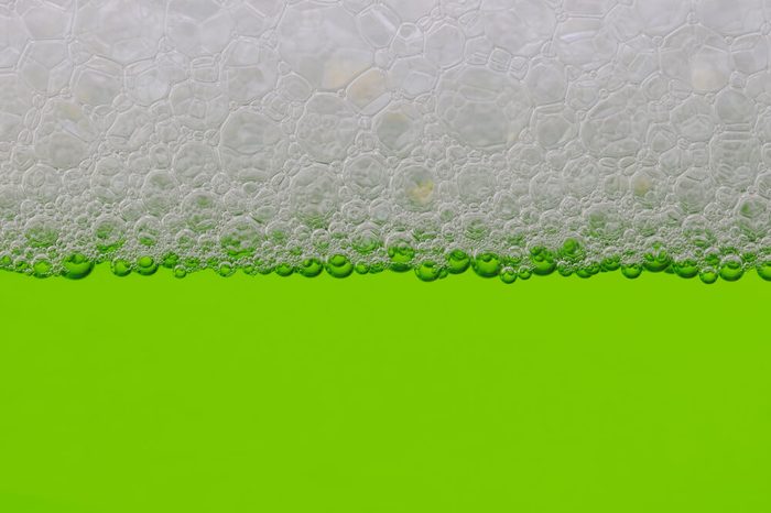 Closeup of a green liquid with a line of bubbles at the top.