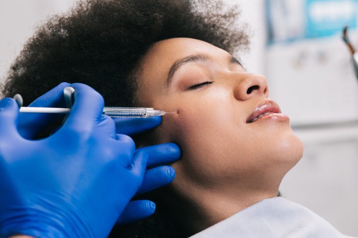 Anti-Aging Treatments | Attractive young African woman is getting a rejuvenating facial injections. She is sitting calmly at clinic. The expert beautician is filling female wrinkles by hyaluronic acid.