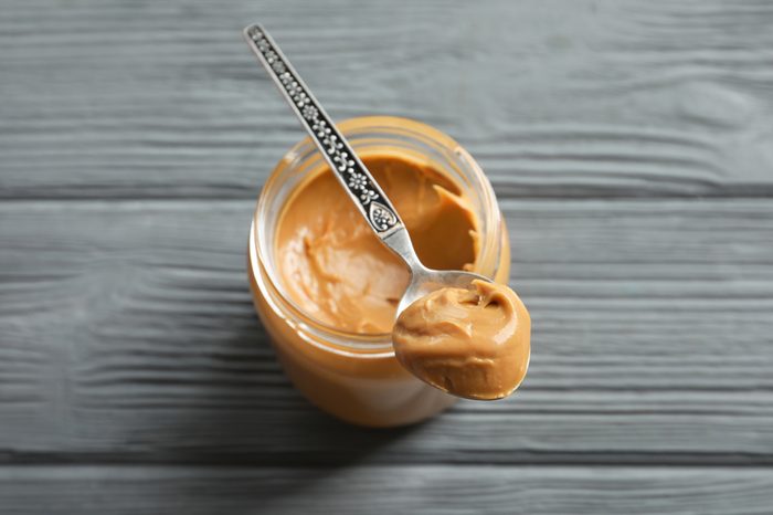 Spoon and glass jar with creamy peanut butter on wooden background