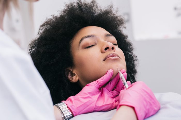 young black African woman is getting a rejuvenating facial injections. botox needle doctor
