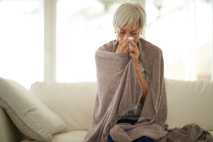 woman blowing her nose at home sick