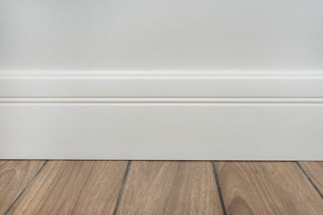 Light matte wall, white baseboard and tiles immitating hardwood flooring