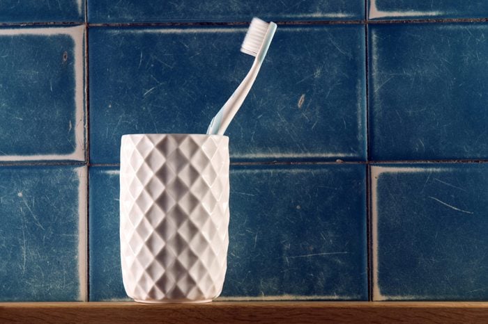 Single toothbrush in white beveled cup against blue tile