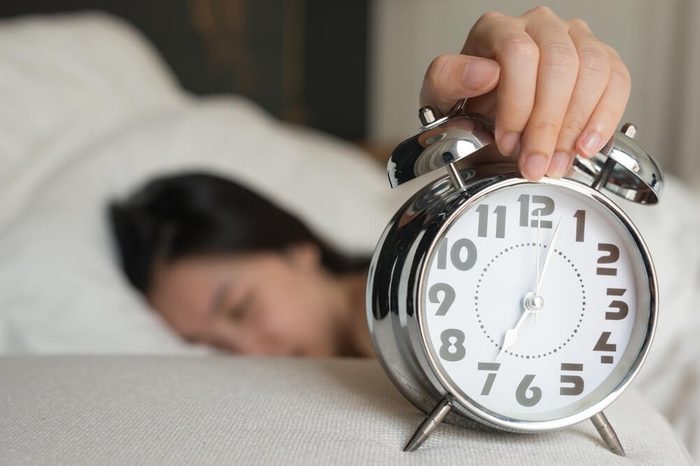Young woman turns off the alarm clock waking up in the morning.