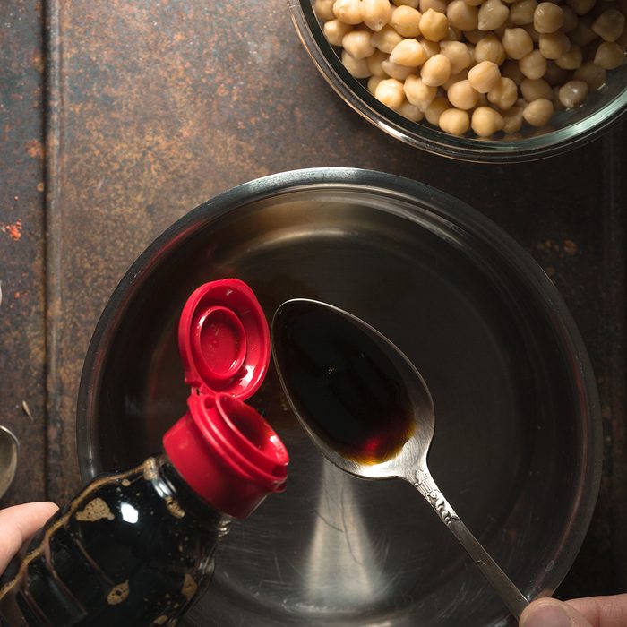 Soy sauce is poured into a spoon over the saucepan