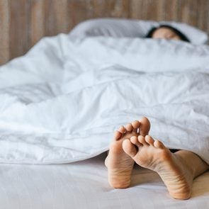 Female feet under blanket flat lay. Female beautiful feet on the bed. Sleeping woman legs under white blanket