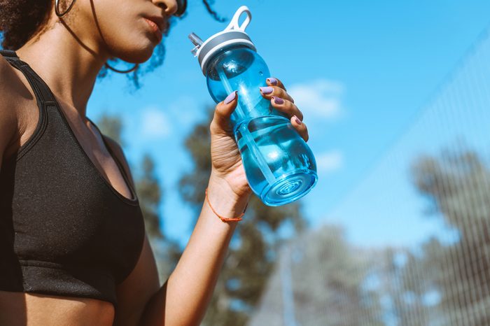 Cropped shot of woman in sports bra drinking from blue water bottle
