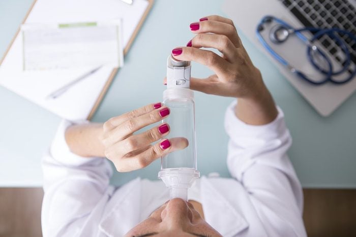 View from above of a female doctor is inhaling the medicament from the pressurized cartridge inhaler placed on an inhalation chamber on a medical demonstration on a desk - Medical respiratory disease