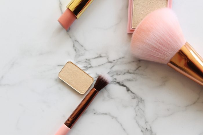 shouldn't be stored in the bathroom | Gold and pink makeup objects against white marble copy space.