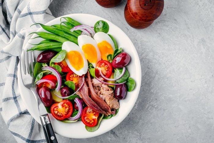 nicoise salad with tuna, anchovies, eggs, green beans, olives, tomatoes, red onions and salad leaves on gray background | foods to avoid before workout