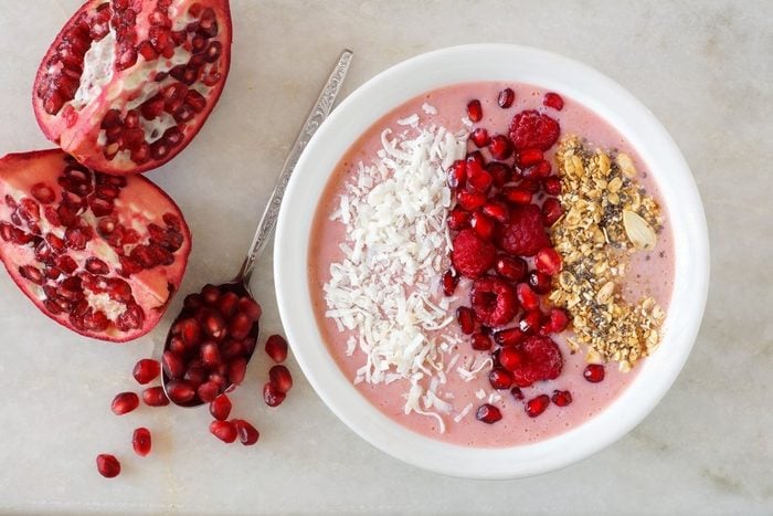 Smoothie bowl with pomegranates, raspberries, coconut and granola, overhead scene on marble | foods to avoid before workout