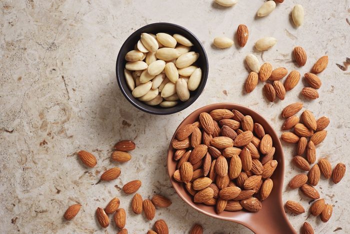 Peeled (blanched) and unblanched whole almonds. Shelled almonds on a spoon with a small black bowl of blanched almonds. | foods to avoid before workout