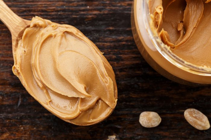 natural organic peanut butter in a spoon isolated, on a wooden background, top view