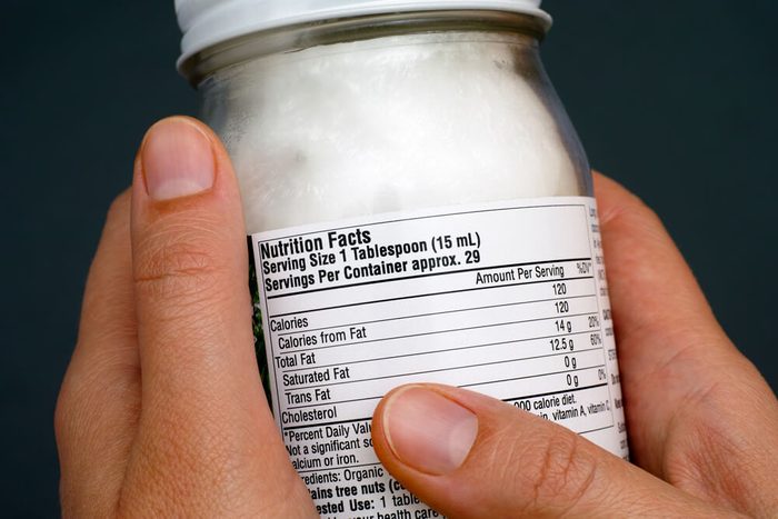 reach your goal weight | Reading a nutrition facts on organic coconut oil jar. Close-up.