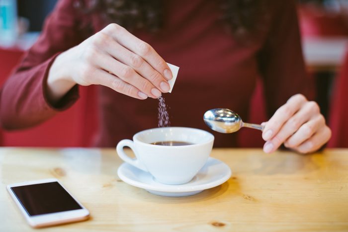 stevia bad for you | Woman's hands pouring sugar into black coffee - girl sitting at the table with espresso and smartphone - blood and glycemic index control for diabetes -excess of white sugar in food concept