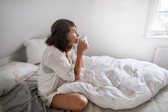 Relaxed young woman drinking coffee in bed