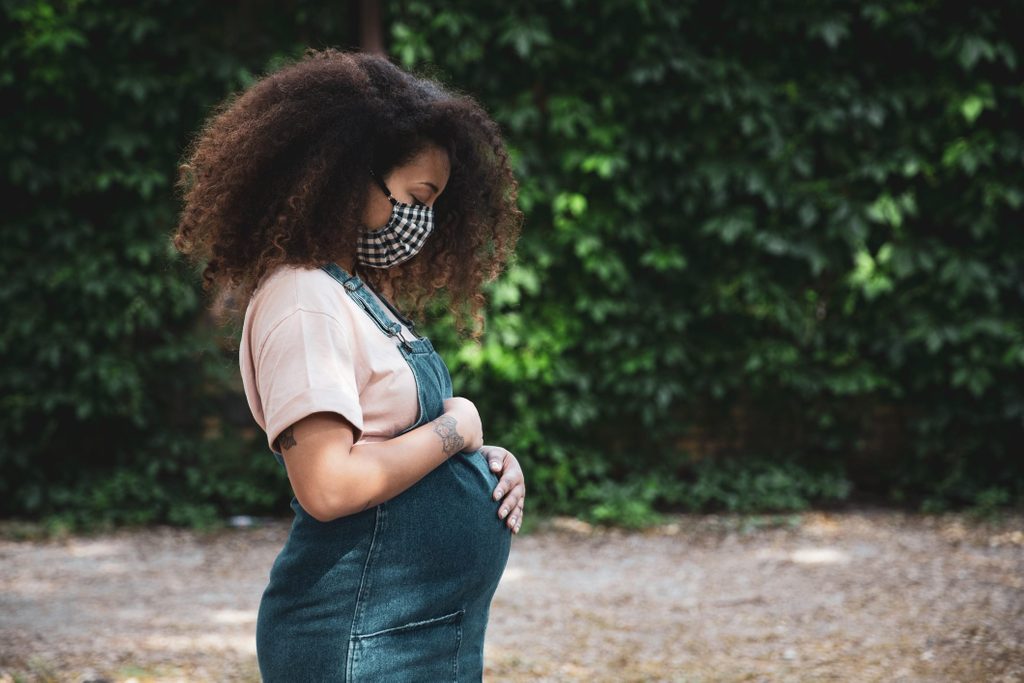 coronavirus pregnancy | Pregnant afro hair woman in the city wearing a cloth protective mask