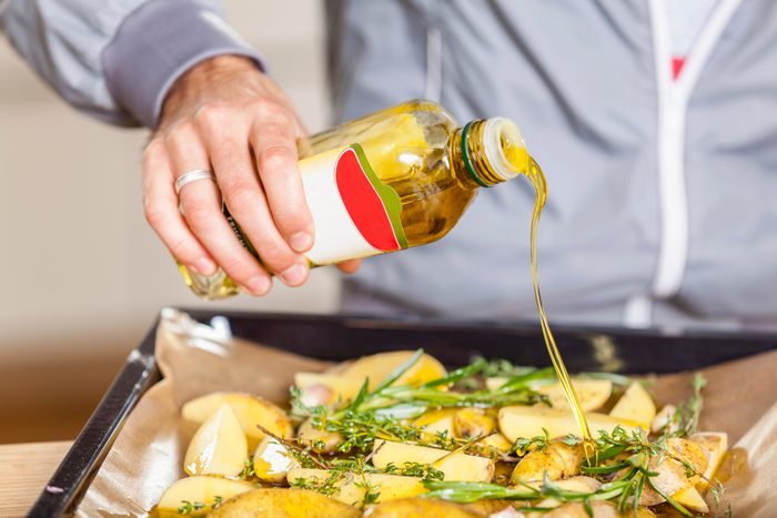 healthiest cooking oils | Pouring oil over potato wedges on baking tray