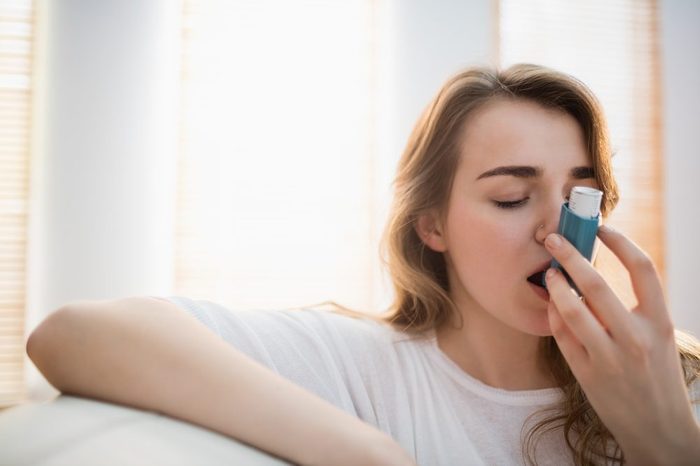 Woman using her inhaler on couch in the living room