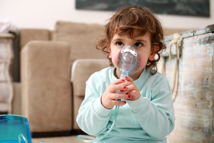 Little girl with asthma problems or allergy using inhaler at home