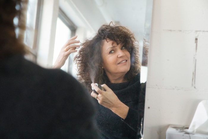 Mature woman applying hair spray in front of mirror