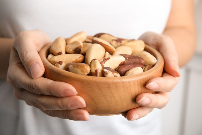 brazil nuts nutrition | Woman holding bowl with Brazil nuts on blurred background, closeup