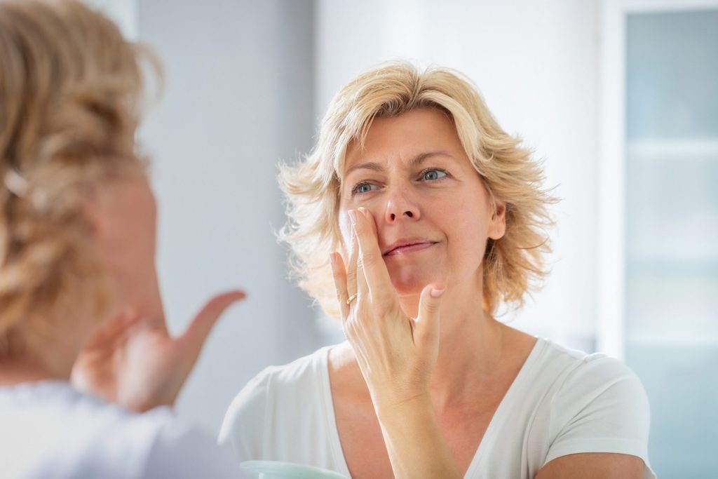 phymatous rosacea | woman looking in the mirror and touching face