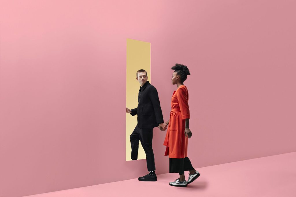 signs you're dating a narcissist | Woman & man holding hands, approaching rectangular opening in coloured wall