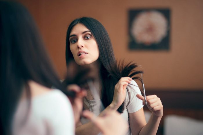 Woman Looking in Mirror Cutting Split Hair Ends