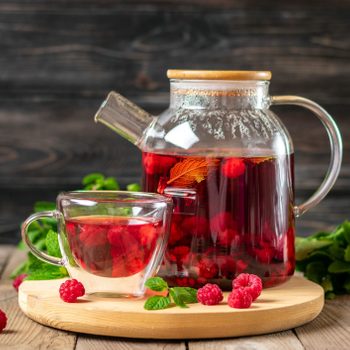 Herbal tea with berries, raspberries, mint leaves and hibiscus flowers in glass teapot and cup on wooden table Medicine for cold Vitamin drink Rustic style