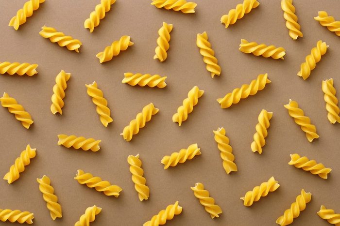 is pasta healthy? | Top view of spiralli pasta pattern.Flat lay raw spilled Italian pasta view from above on neutral background. Repetition concept.