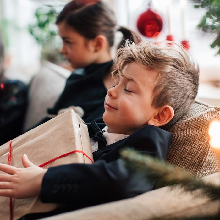 Smiling boy holding Christmas present while sitting with family in living room