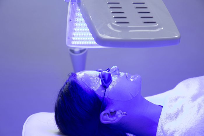 blue light therapy for acne | Young woman having blue LED light facial therapy treatment in beauty salon. Beauty and wellness