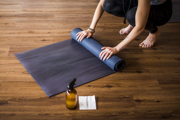 Woman Rolling Up Yoga Mat With Sanitizer Nearby