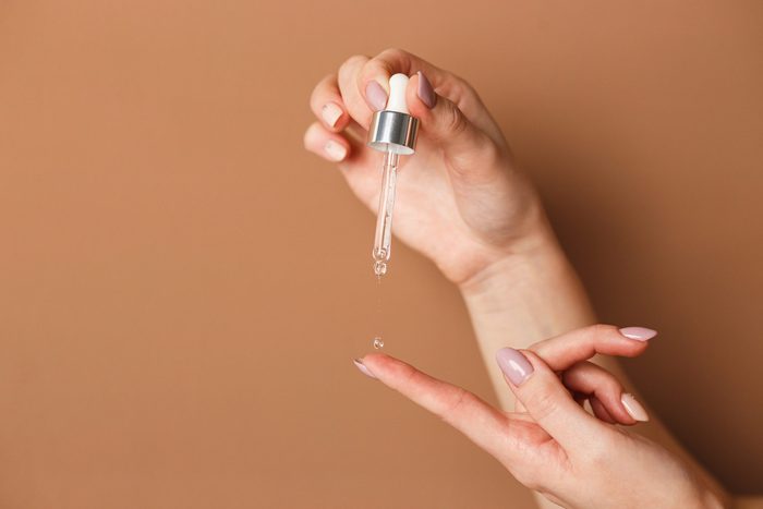 niacinamide | Hands Of Cropped White Woman Holding Cosmetic Serum Pipette On The Orange Background
