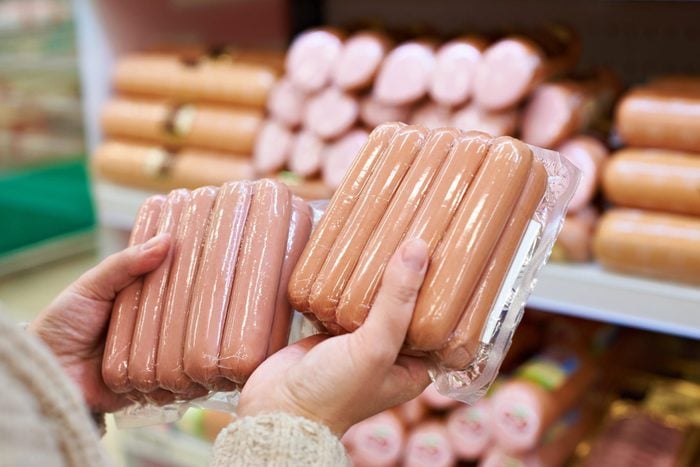 foods and drinks that cause migraines | processed meat | Woman Chooses Sausages In Vacuum Package At Store