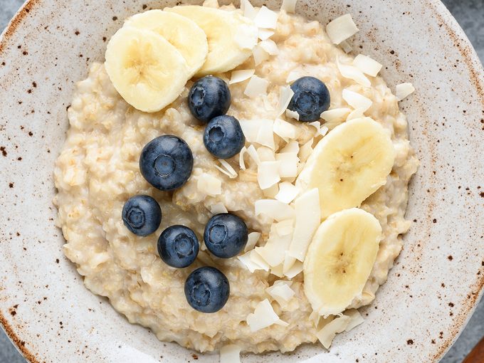 Oatmeal,porridge,bowl,with,banana,,blueberries,,coconut,on,concrete,background,