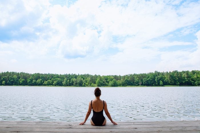 Woman,sitting,on,wooden,dock,looking,at,lake,in,sunny