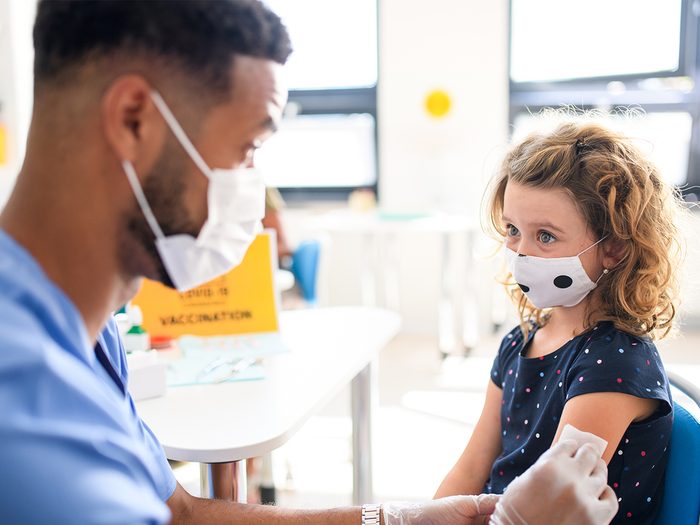 Photo of a health care worker wearing a mask giving a COVID vaccine to a young girl, who is also wearing a mask and looking at him. This photo accompanies a story on COVID vaccines for kids in Canada.