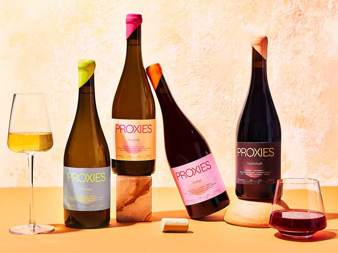 A image of four bottles of Acid League's Proxie non-alcoholic wine, surrounded by wine glasses.