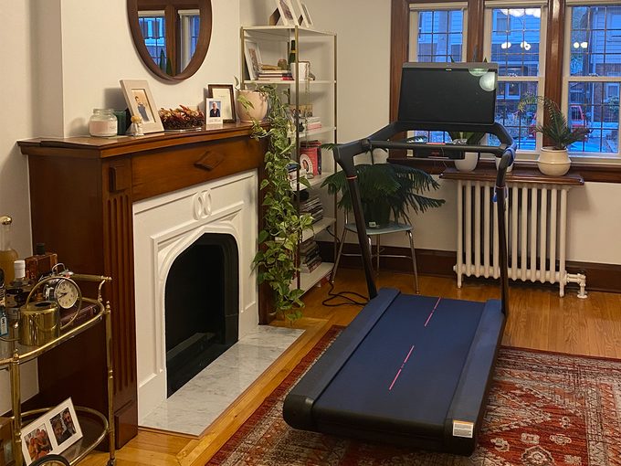 Peloton Treadmill Canada: A photo of the Peloton Tread set up in the living room of an old home, next to a fireplace and facing the window. 
