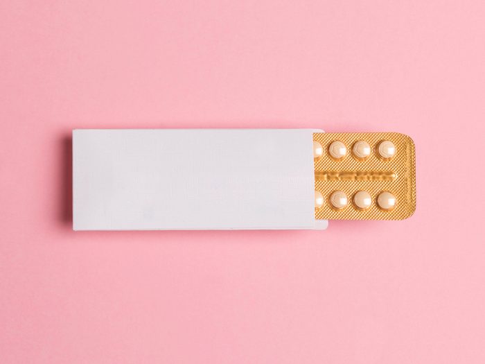 Image of a birth control package with the pill pack pulled out on a pink background for a story on whether Birth Control Make Your Boobs Bigger Feature