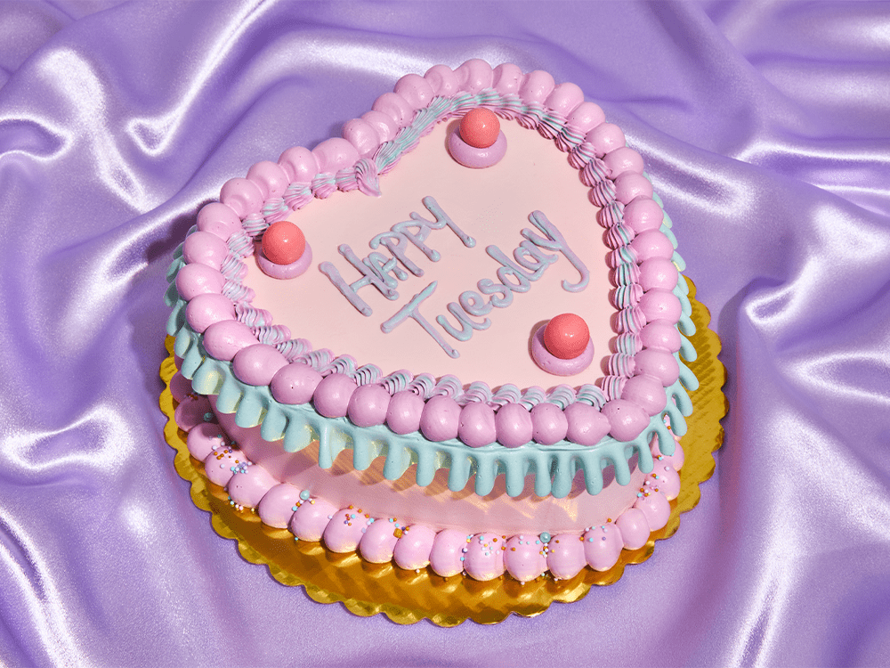 a heart shaped cake that reads happy tuesday on a purple satin backdrop | Small Wins Hero