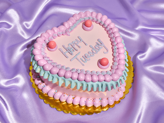 a heart shaped cake that reads happy tuesday on a purple satin backdrop | Small Wins Hero