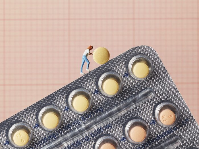 birth control pill | miniture of a woman pushing a birth control pill up a hill of pills