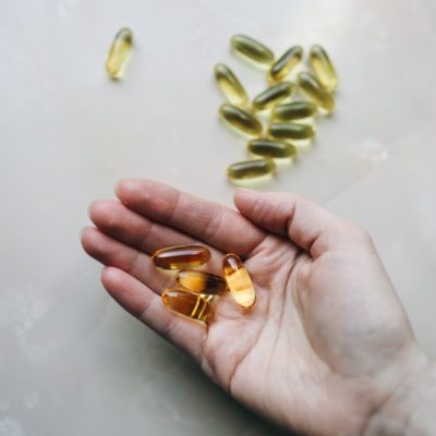 Omega 3 pills in woman's hand on marble background. Healthy diet supplements. Fish oils for vegans food.