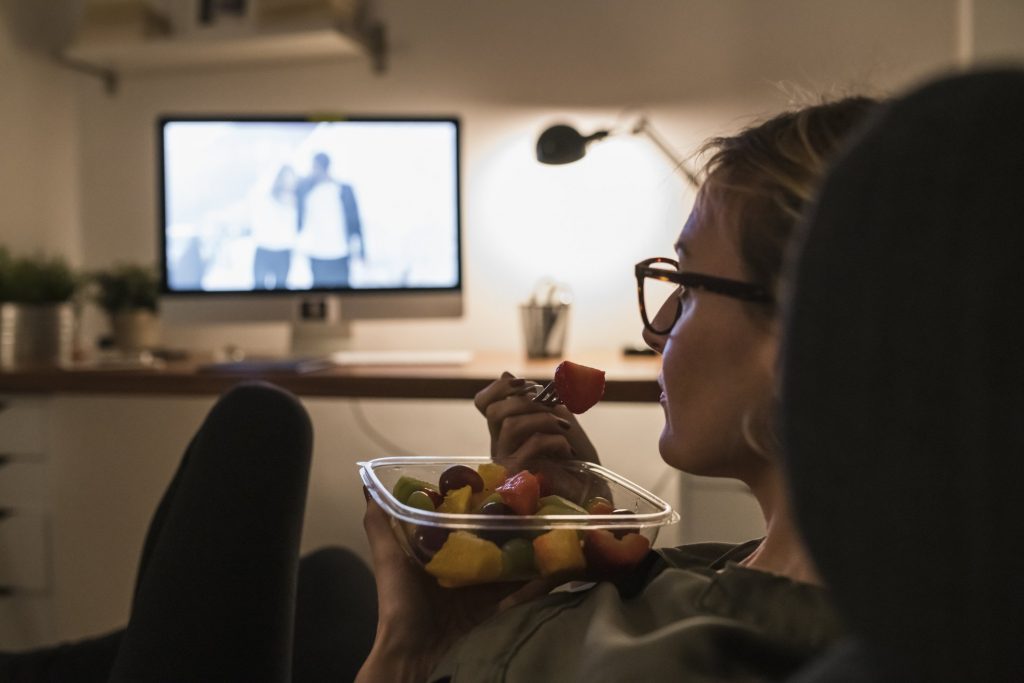 work from home | woman eating a snack and watching a movie at home after work